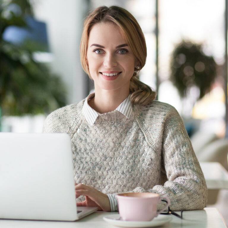 Forensic Accounting A woman, sitting at a table, is smiling while using a laptop with The Official Page Template.