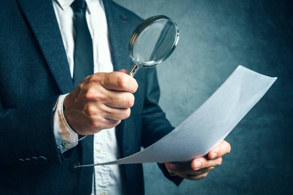 Forensic Accounting A man in a suit conducting a financial investigation with a magnifying glass.